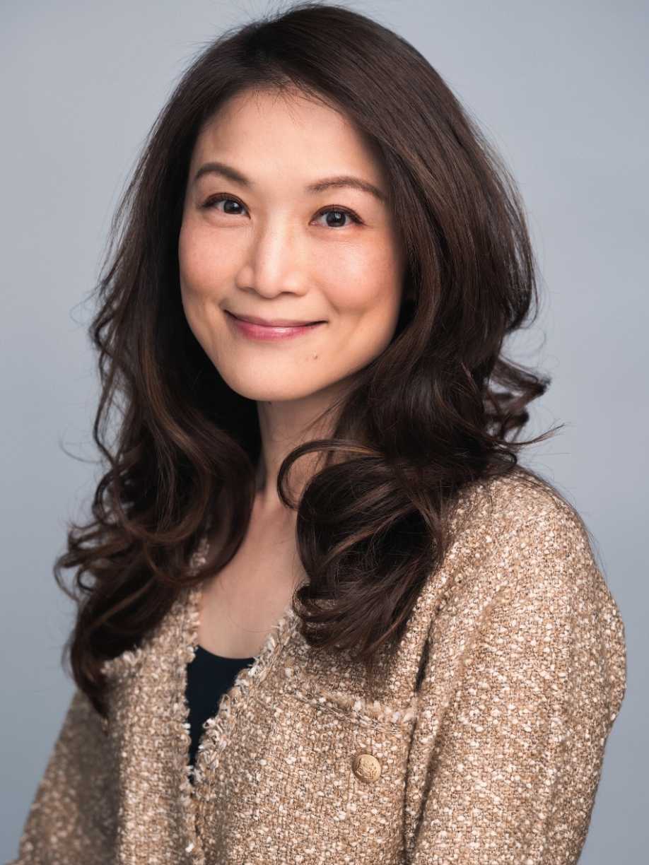 Alycia Szeto picture. It shows a woman with long hair smiling at the camera, wearing a textured jacket on a grey background.